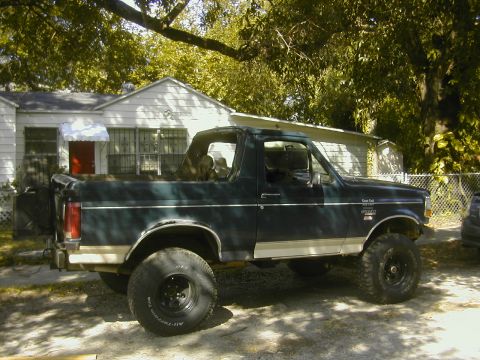 1993 Ford Bronco - Two-tone green and white lifted full-size Ford Bronco with hardtop and large tires parked in a residential yard.