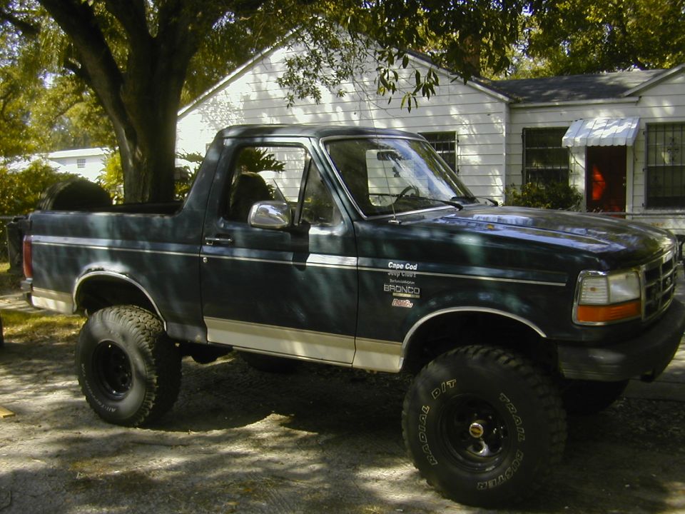 Lifted dark green Ford Bronco with top removed, side view in driveway
