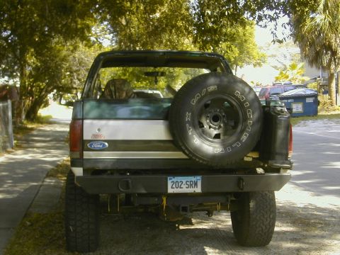 1993 Ford Bronco - Rear view of a lifted green and tan two-tone Ford Bronco with the top and rear glass removed, showing a bed-mounted Michelin LTX M/S spare…
