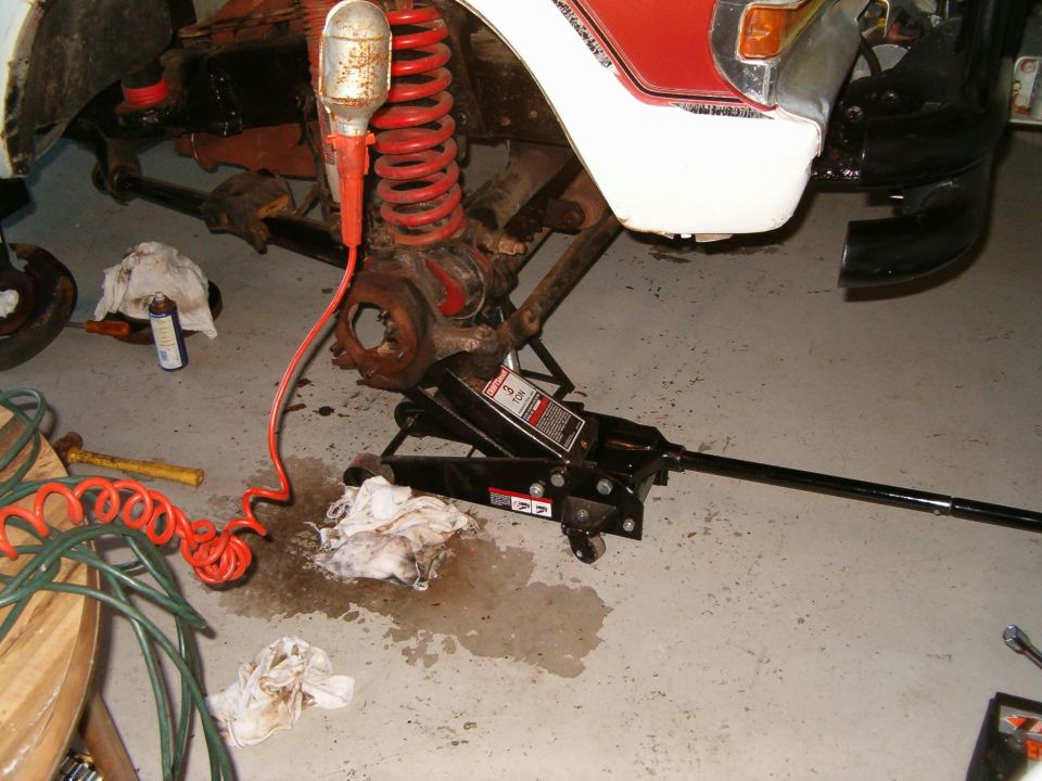 Vehicle suspension with red coil springs, jack, and tools on a concrete floor