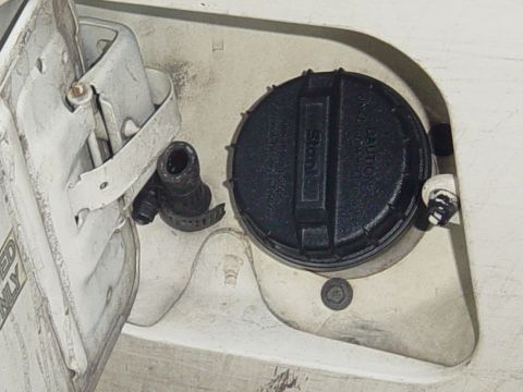 1989 Ford Bronco - Close-up of a vehicle's fuel filler neck and cap, showing a black cap with caution text and a rubber hose.