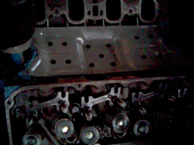 Disassembled V8 engine with exposed valve springs, cylinder head, valley pan and intake manifold in dim lighting