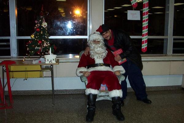 Santa Claus sitting with a man standing behind him, Christmas decorations visible