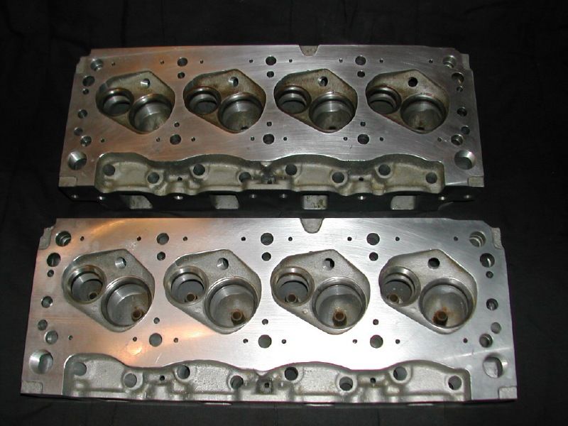 Pair of bare cast-iron V8 cylinder heads shown chamber-side up on black background