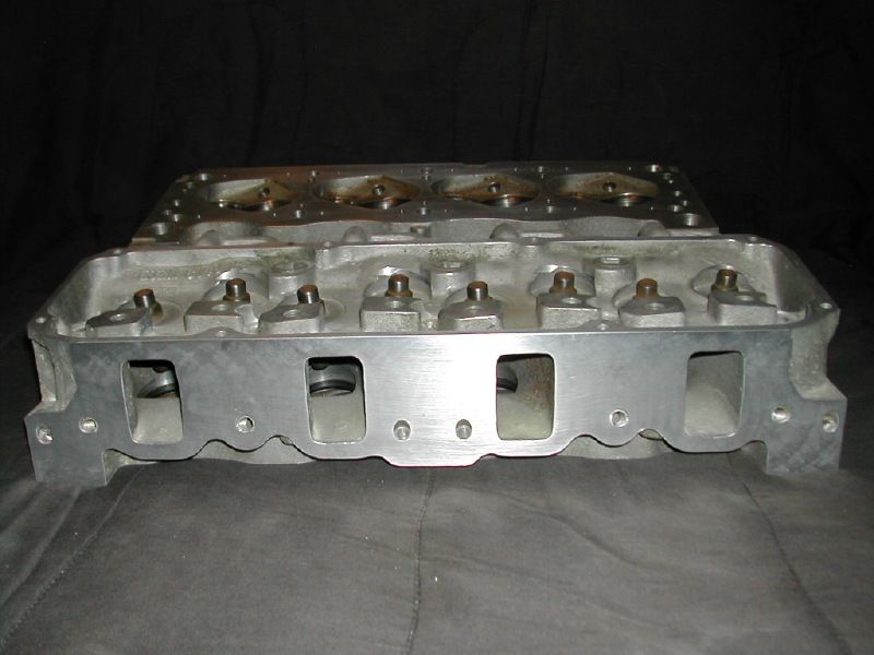 Two bare aluminum V8 cylinder heads on gray cloth, showing rectangular intake ports and machined surfaces