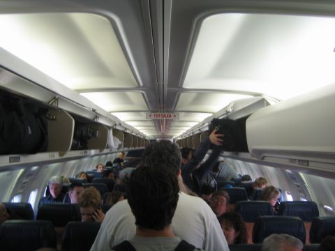 1968 Ford Mustang - View inside an airplane cabin during boarding, showing passengers and luggage in overhead bins.