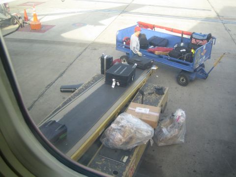 1968 Ford Mustang - Baggage is being loaded onto a cart and conveyor belt on the airport tarmac.