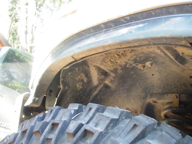 Muddy wheel well and frame of an off-road truck above a mud-terrain tire