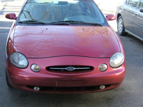 1998 Ford Taurus - The front end of a red Ford Taurus is visible, parked on a street next to another vehicle.