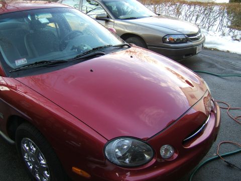 1998 Ford Taurus - A red 1998 Ford Taurus is parked next to a gold sedan in a driveway during winter.