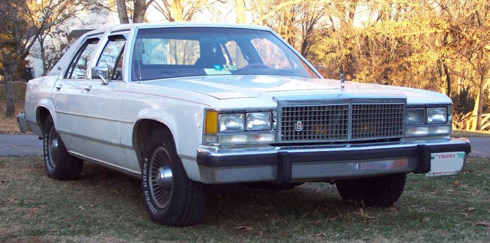 White sedan parked on grass, front quarter view. License plate visible