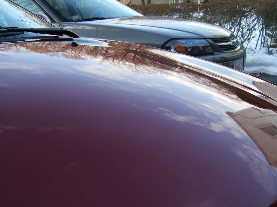 Red car hood reflecting sky and trees, with a silver car behind