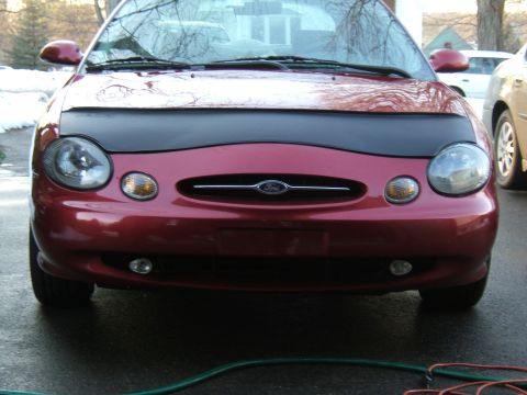 1998 Ford Taurus - The front of a red Ford Taurus is shown, a black car bra and the Ford emblem on the grille.