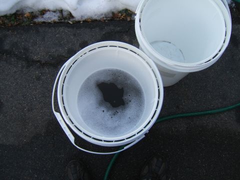 1998 Ford Taurus - Two buckets sit on asphalt near snow, one containing soapy water, with a green hose nearby.
