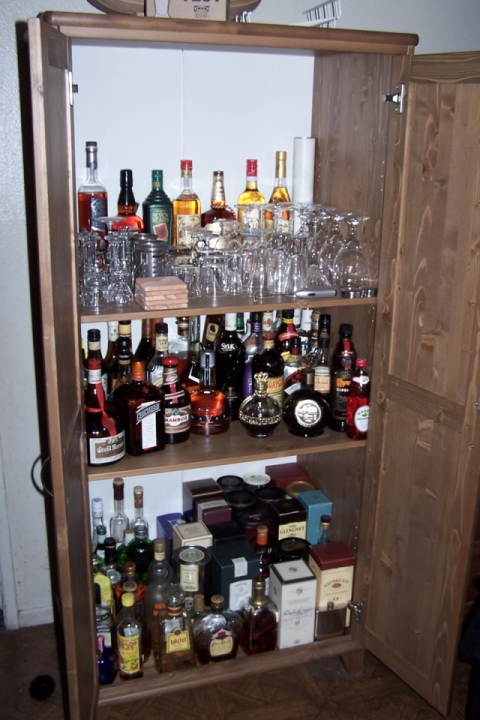 1990 Ford Bronco - A wooden liquor cabinet is filled with various bottles of alcohol and drinking glasses.