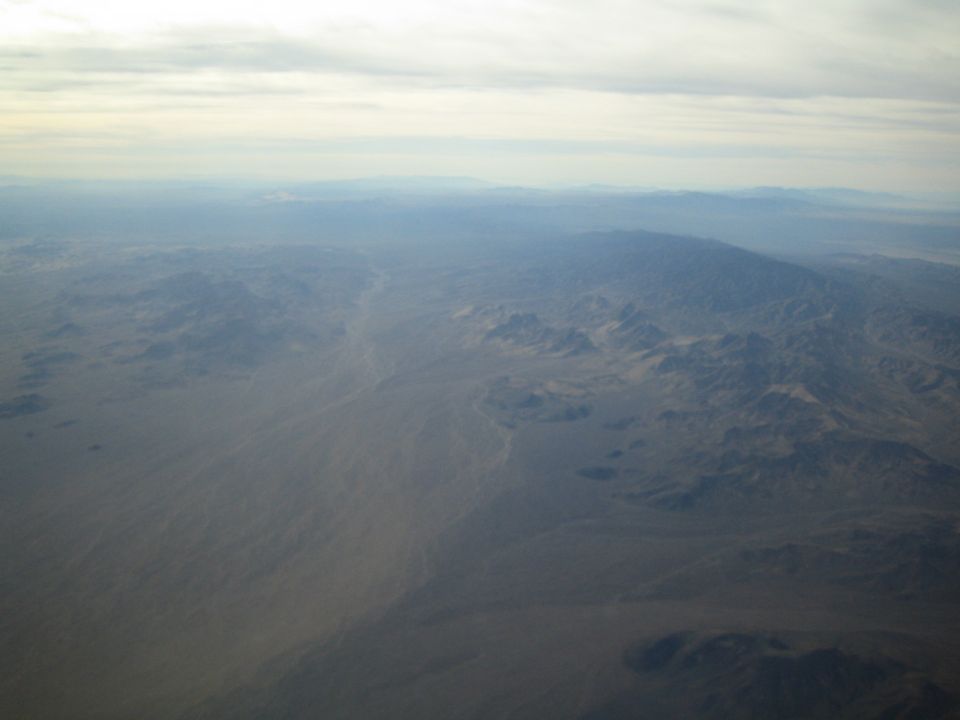 Aerial view of a vast, hazy desert landscape with mountains in the distance