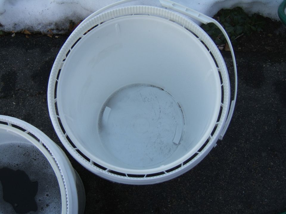 Two white buckets, one with soapy water, sit on asphalt next to snow