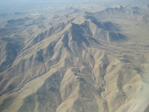 1968 Ford Mustang - This aerial photograph captures a vast expanse of desert mountains, characterized by their dry, rocky terrain and winding ravines.