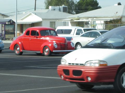 1968 Ford Mustang - A red 1940 Ford coupe is parked in a lot with other cars visible.