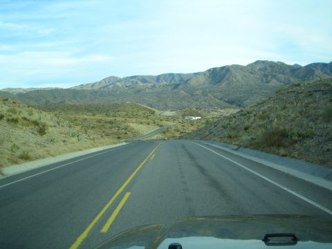 1968 Ford Mustang - A road winds through a dry, mountainous terrain under a partly cloudy sky.