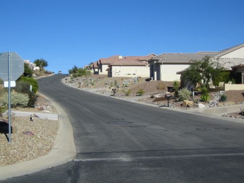 1968 Ford Mustang - A car ascends a street lined with desert landscaping and homes under a clear blue sky.
