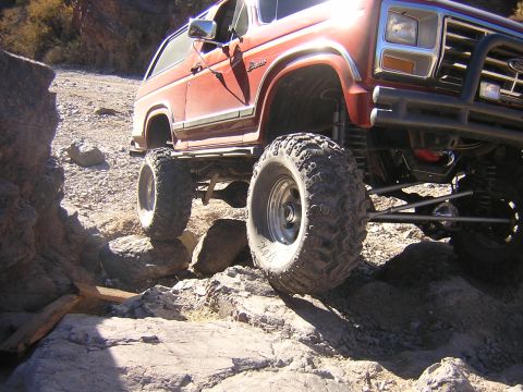 1984 Ford Bronco - Modified red Ford Bronco tackling a difficult off-road trail.