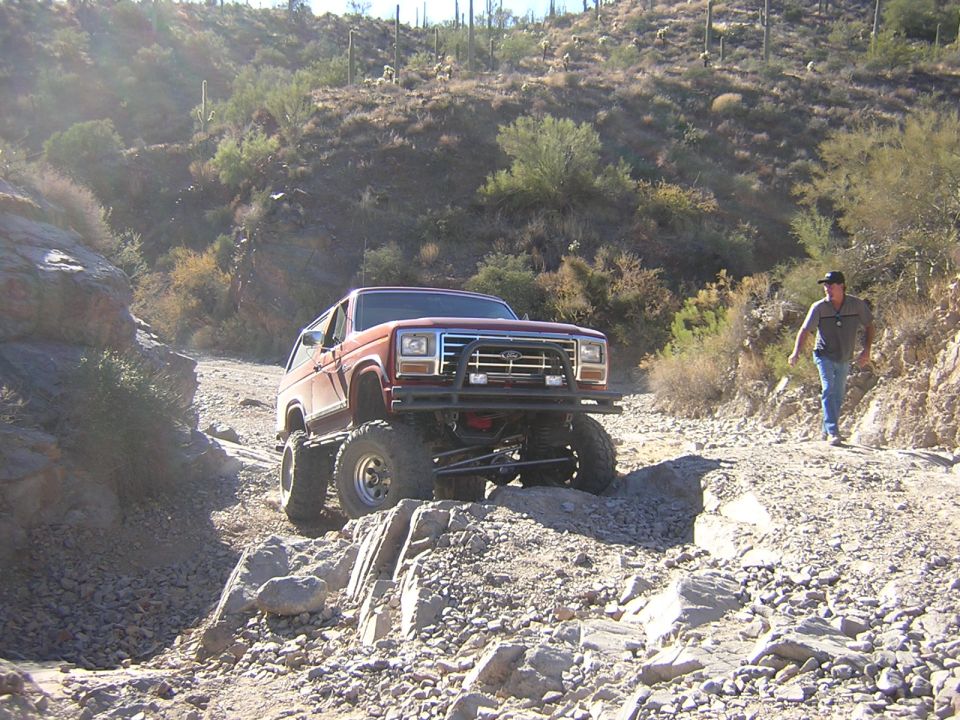 Red Ford Bronco on rocky trail, guy walking behind it