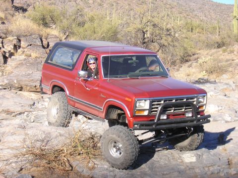 1984 Ford Bronco - Red Ford Bronco navigating rocky terrain in a desert environment.