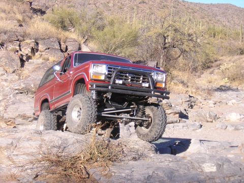 1984 Ford Bronco - This modified SUV is navigating a rocky trail in a dry, desert environment.