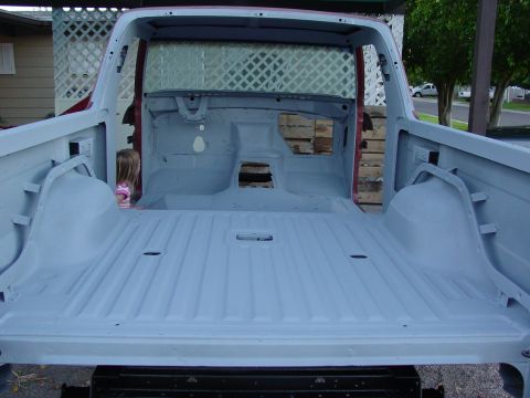 1979 Ford Bronco - The interior of a pickup truck bed and cab, primed and ready for paint, with a child peeking from the cab.