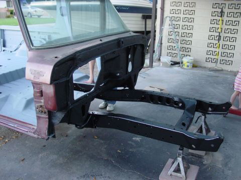 1979 Ford Bronco - The chassis and frame of a vehicle are shown, with the body and windshield partially visible, resting on jack stands.
