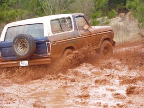 1978 Ford Bronco - A muddy 1978 Ford Bronco navigates a challenging off-road terrain.