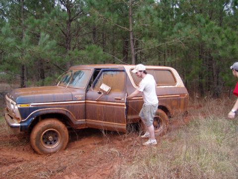 1978 Ford Bronco - A man opens the door of a mud-covered 1978 Ford Bronco stuck in a wooded area.