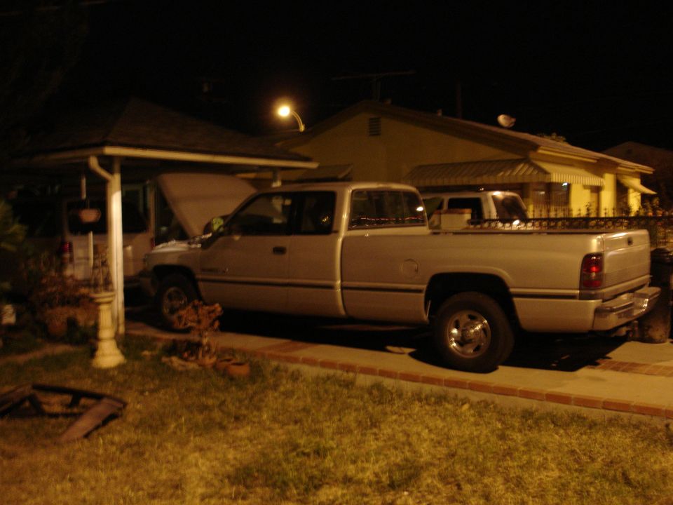 Silver pickup truck with hood up parked in driveway at night. Another truck is behind it