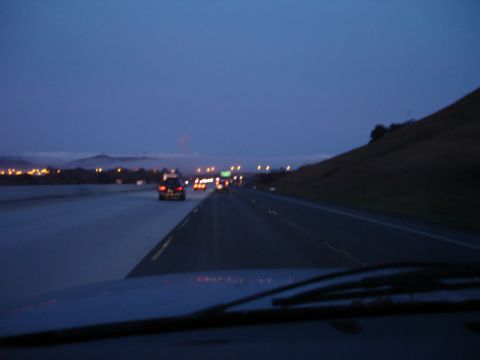 1992 Ford Taurus - Cars drive on a highway as dusk settles, with distant city lights visible on the horizon.