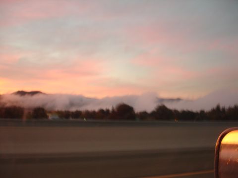 1992 Ford Taurus - The side mirror of a vehicle captures a misty mountain range under a pink and orange sunrise sky.