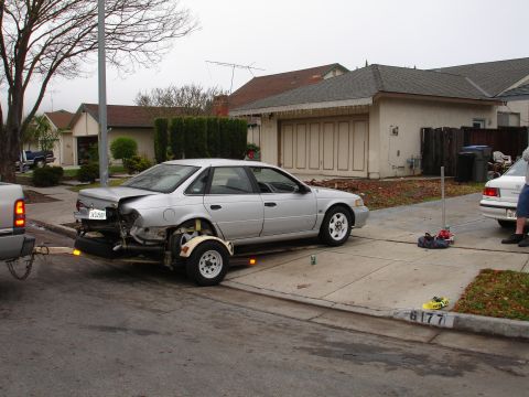 1992 Ford Taurus - A silver sedan is being towed on a trailer, showing significant rear damage.