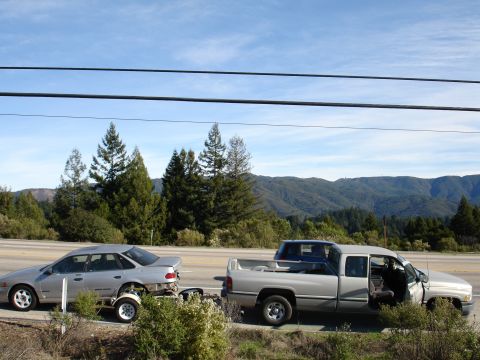 1992 Ford Taurus - A pickup truck tows a sedan on a trailer, with another vehicle visible in the truck's bed.