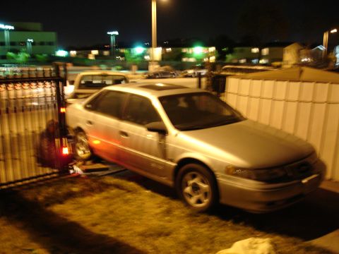 1992 Ford Taurus - A silver sedan is parked near a fence with a truck in the background at night.