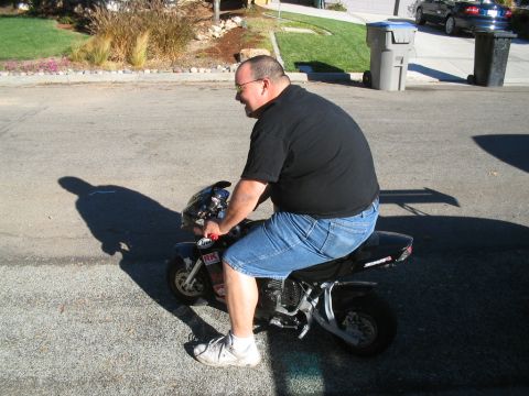 1995 Ford Probe - A man is seen riding a small motorcycle down a residential street.