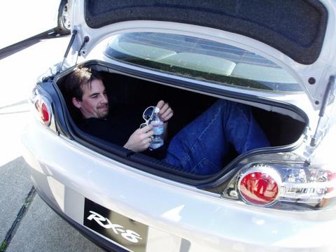 1995 Ford Probe - A man relaxes in the trunk of a silver Mazda RX-8, with the Supermotors logo visible on the bumper.