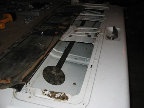 1995 Ford Bronco - The interior of a vehicle reveals an open storage area with a metal shaft and flange, showing signs of wear and rust.