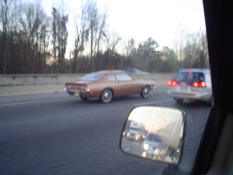 1966 International School Bus - A brown coupe with a distinctive fastback roofline drives on the highway, with other vehicles visible.