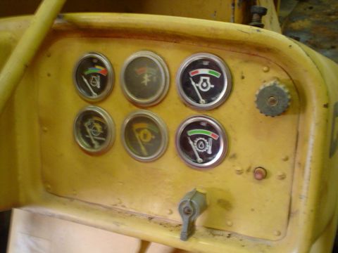 1966 International School Bus - Close-up of a yellow dashboard multiple gauges and a lever, likely from heavy machinery.