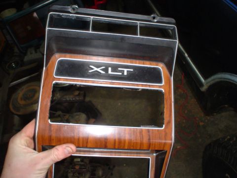 1984 Ford Bronco - Dashboard trim piece with 'XLT' badging and woodgrain accents is being held.
