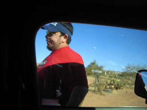 1968 Ford Mustang - A man wearing a red shirt and blue visor stands outside a vehicle, with a desert landscape visible in the background.