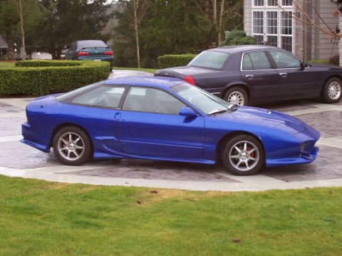 1993 Ford Probe - A blue 1993 Ford Probe is parked on a wet driveway next to a dark sedan.