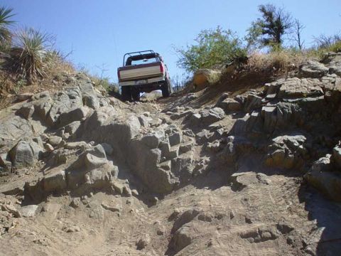 1989 Ford Bronco - A Ford Bronco navigates a challenging rocky terrain under a clear blue sky.