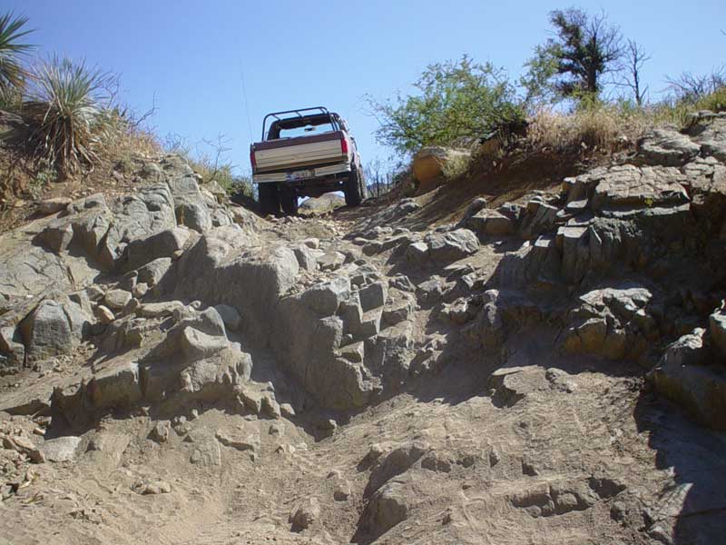 Brown and white Ford Bronco driving up a rocky hill