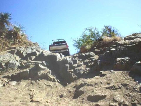 1989 Ford Bronco - A truck navigates a steep, rocky incline under a clear blue sky.
